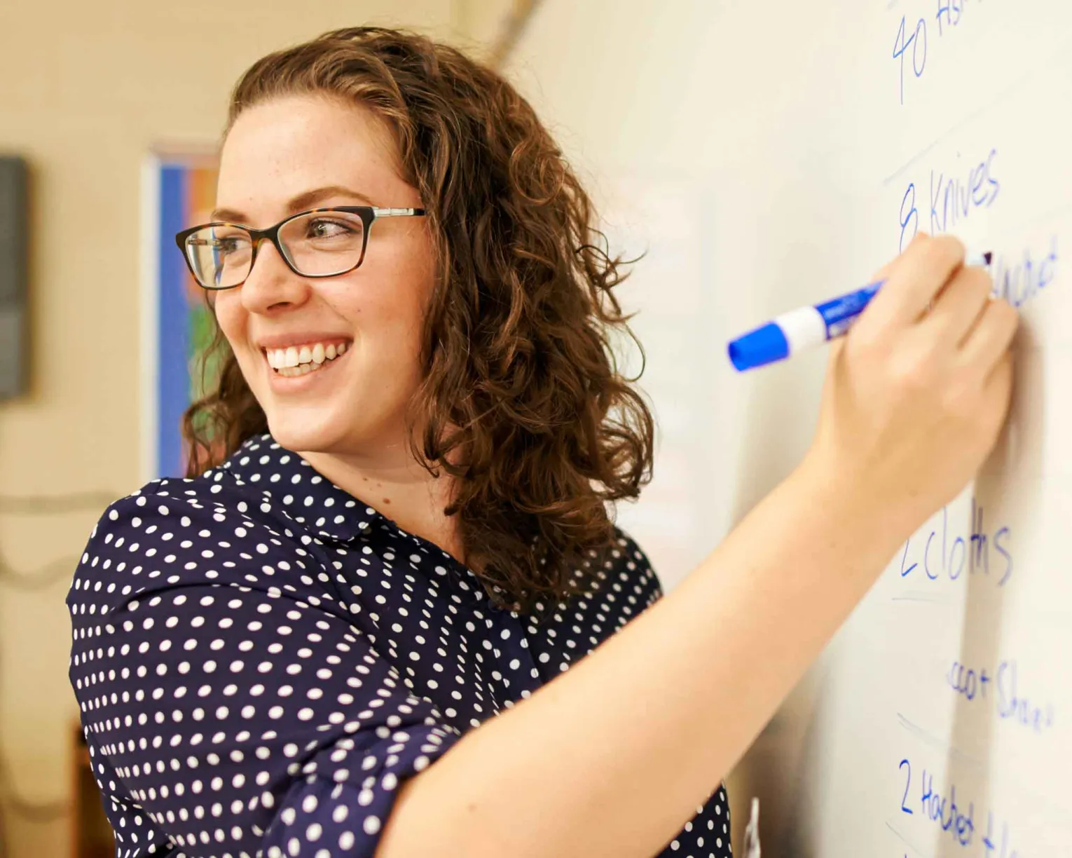 A smiling female teacher writes on a whiteboard