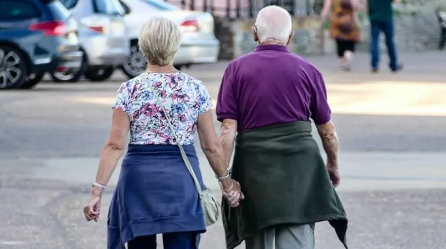 A retired couple walks hand in hand away from the camera